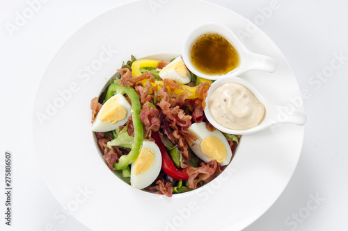 Fresh Caesar Salad with Deep-fried Bacon and Boiled Eggs & Mayonnaise on White Porcelain Circle Dish, Isolated on White Background with Shadow. Close-up Top View, Selective Focus at Food.