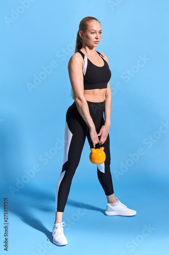 pleasant young sportswoman working out with weight. full length side view photo. isolated blue background. hobby, interest, lifestyle