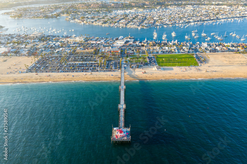 Aerial view from above over Newport Beach in coastal Orange County, California on a sunny day from above with the ocean, pier and harbor in view.