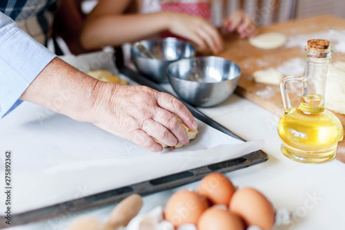 Cooking process. Family is cooking in cozy home kitchen. Eggs, oil, baking paper and ingredients are on table. Graceful hands of senior woman and child prepare autumn pastries for dinner