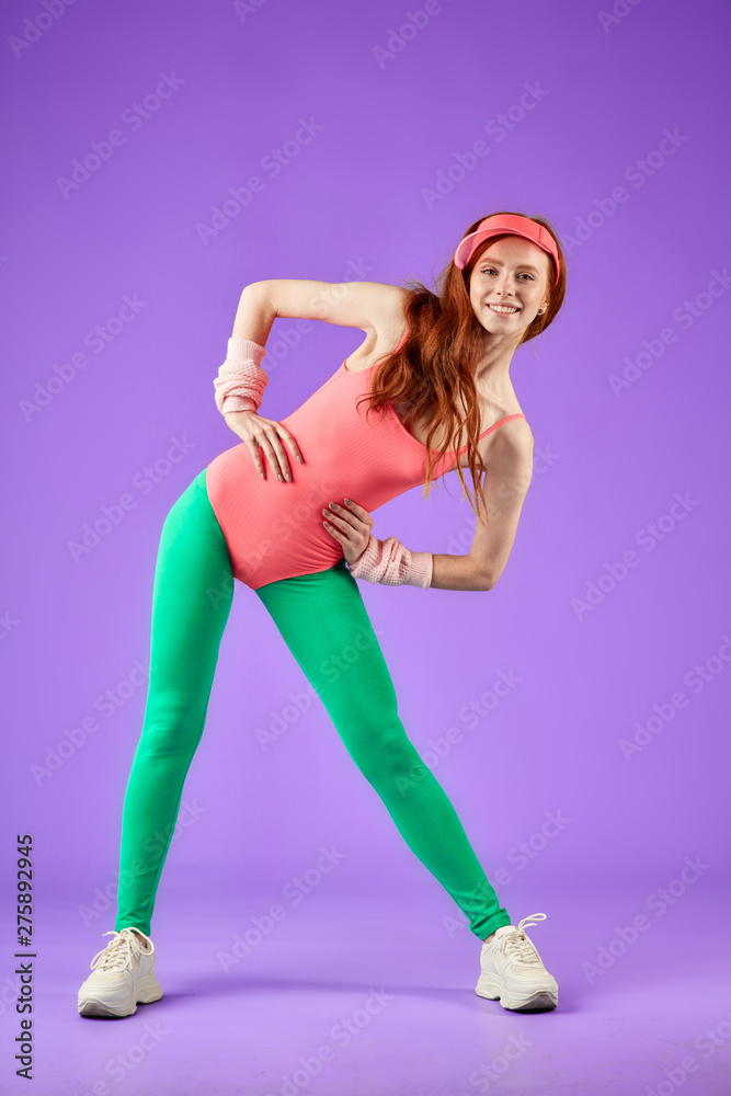 red-headed girl full of energy and inner light, in perfect body shape, leans right, legs apart, wears 80s retro style pink bodysuit and green leggins