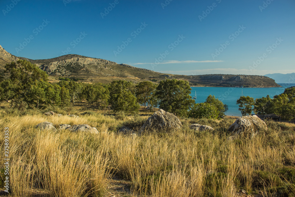 Greece golden scenery landscape of rural hill land meadow and stones foreground and mountains and Mediterranean sea bay background 