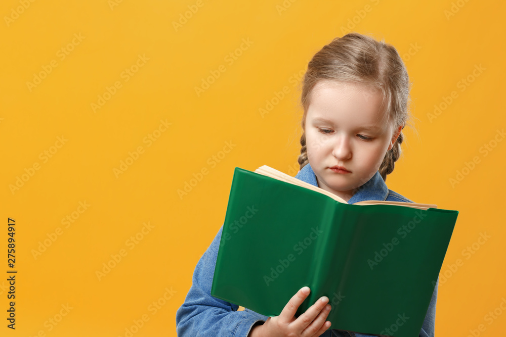 Little student girl in denim shirt on yellow background. The child is reading a book. The concept of education and school. Little student girl in denim shirt on yellow background. The child is reading a book. The concept of education and school.