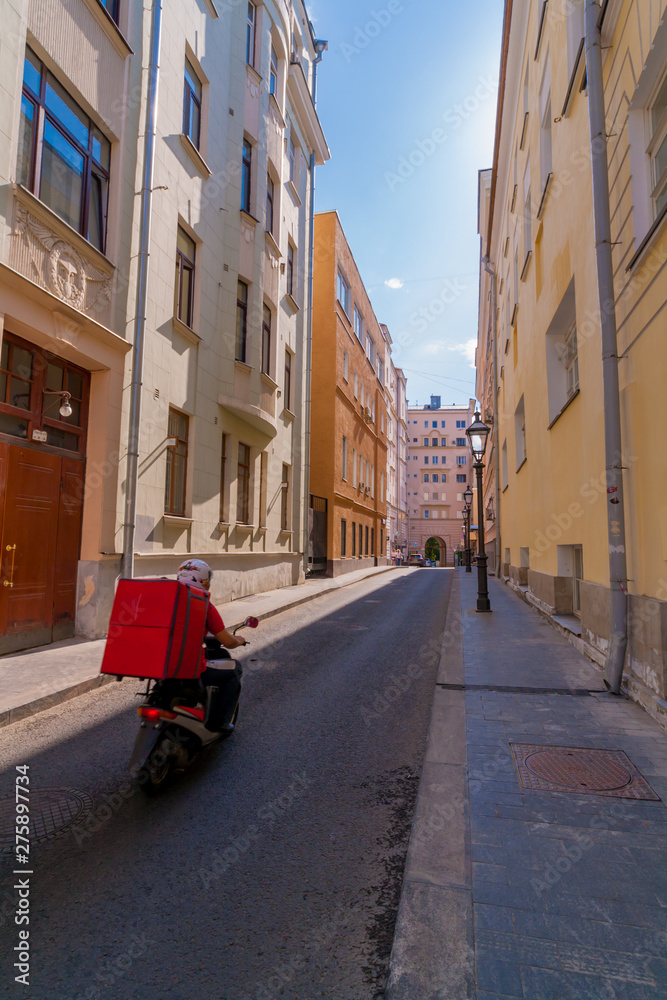 cityscape of narrow street with colorful houses and biker on scooter. food delivery in the city