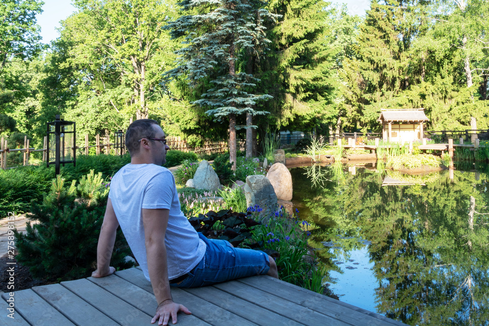 Fototapeta premium Young attractive man meets a dawn while sitting on a wooden pier in front of a small pond