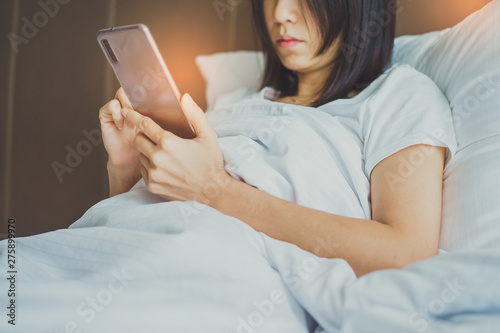 Asian Girl in bed room on the bed with the mobile phone.Closeup portrait of young sleepy exhausted woman lying in bed using smartphone,