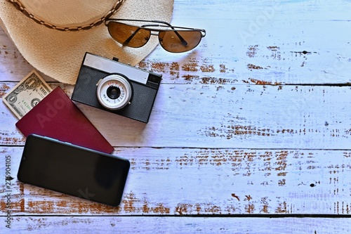 Items for summer vacation: a camera, passport,smartphone, money, hat, sunglasses. Wooden background, top view with Copy space. Beautiful summer concept for travel and summer vacation-holidays.