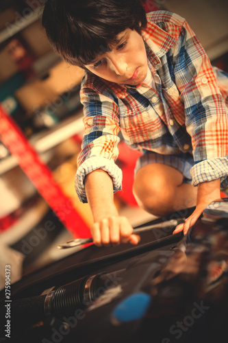 Boy car mechanic with a wrench bent on the engine of the car