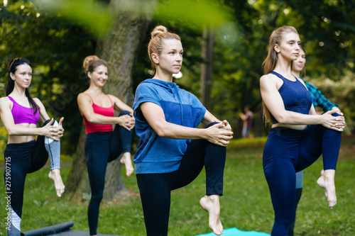 Yoga or pilates at park, group of mixed age women doing different pose while standing in morning time. Teamwork, sport, good mood and healthy life concept. Seria photo with real people models.