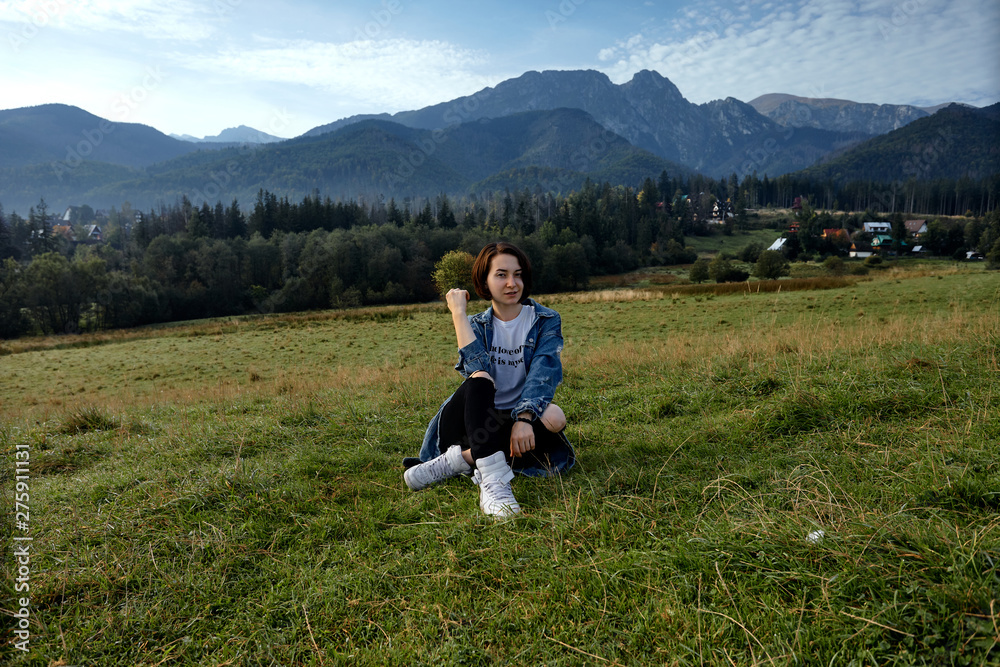 Fototapeta premium Girl sitting on grass. Mountains as a background