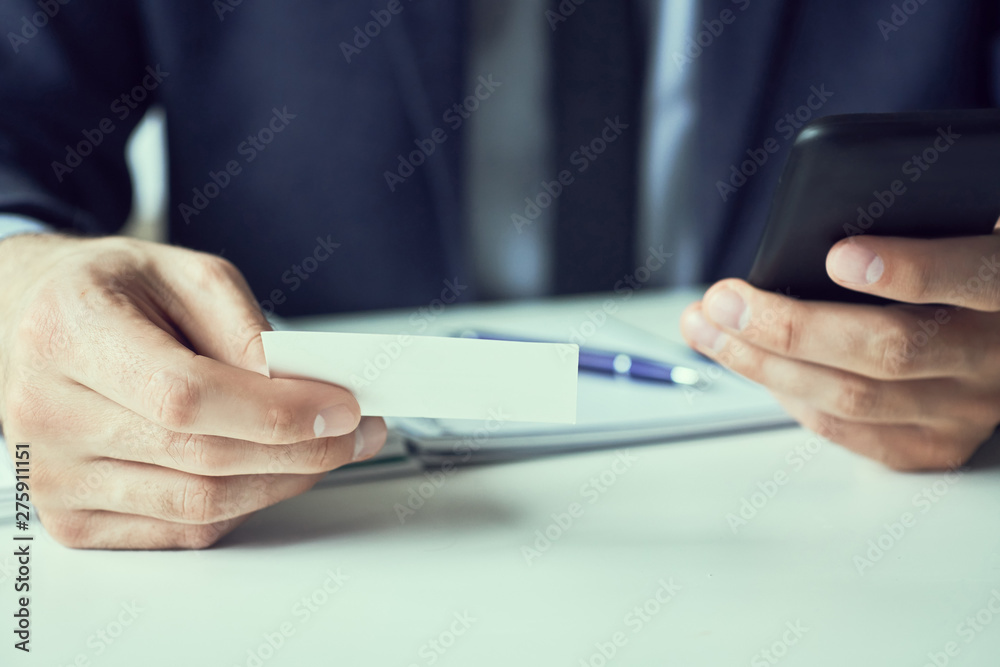 Businessman holding blank business card and dialing numbers on mobile phone Businessman holding blank business card and dialing numbers on mobile phone