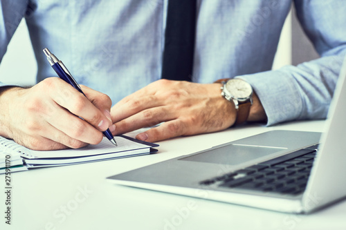 Businessman hand writing note on a notebook. Business man working at office desk. Close up of empty notebook on a blackboard with office supplies.