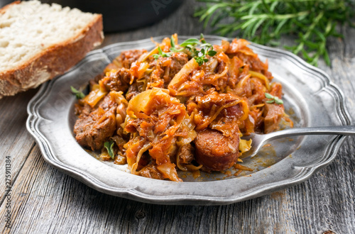Traditional Polish kraut stew bigos with sausage, meat and mushrooms as closeup on a pewter plate on an old wooden table  photo