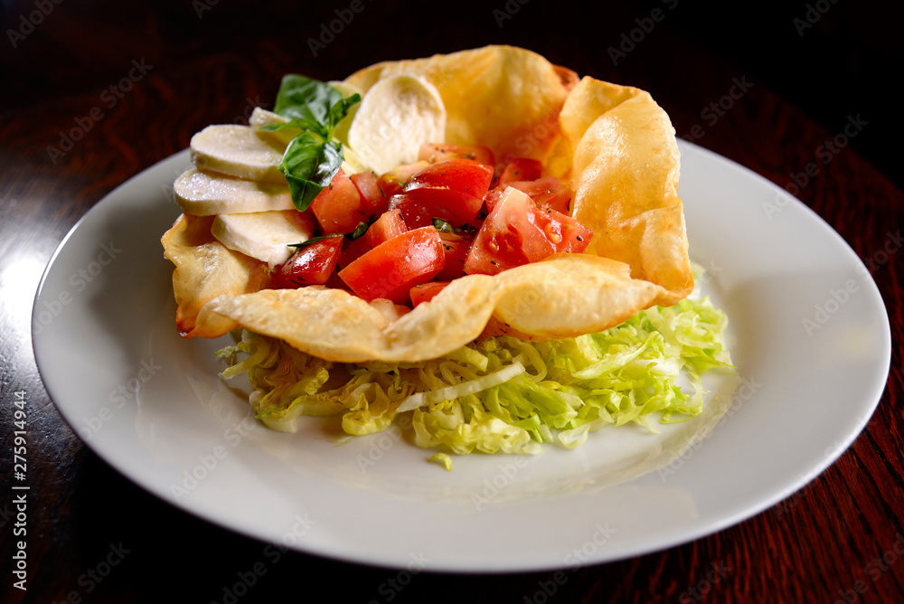 Salad of tomatoes, mozzarella and basil (caprese) in fried tortilla on white plate