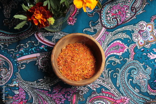 Fototapeta Naklejka Na Ścianę i Meble -  Zafaran spice in wooden bowl on colorful background with  marigold flowers bouquet 