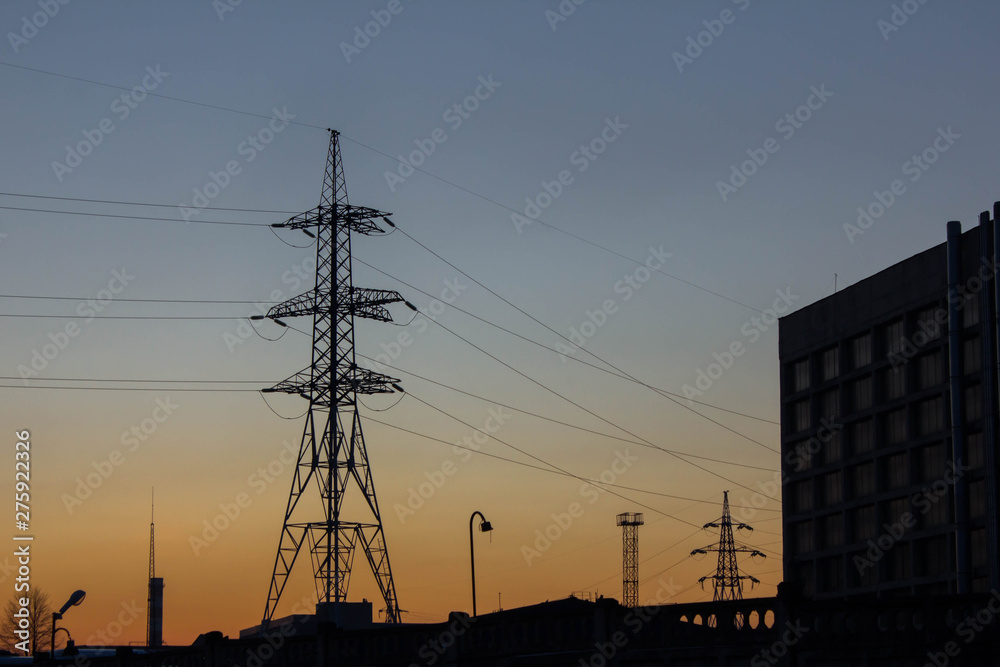 Silhouette of a pylon of a high voltage power line and a plant in the evening light of the setting sun. Electricity distribution, industry and manufacturing. Industrial landscape. Voltage transmission