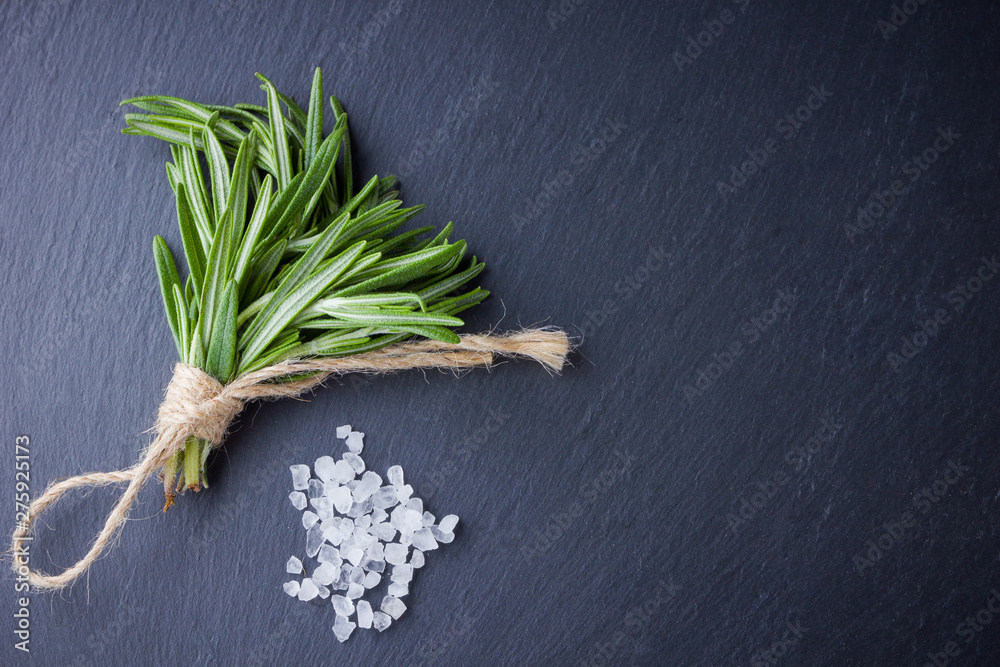 Rosemary bundle tied with twine on a black background. Fresh rosemary and salt on slate stone. Herbs for cooking meat dishes with copy space. Top view Rosemary bundle tied with twine on a black background. Fresh rosemary and salt on slate stone. Herbs for cooking meat dishes with copy space. Top view