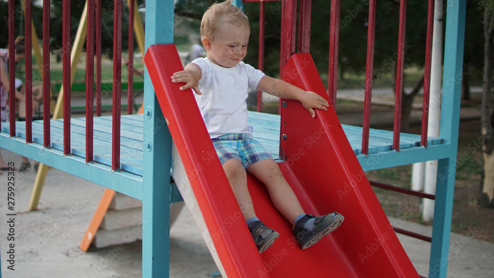Obraz premium Smiling little boy riding on the slide on the playground
