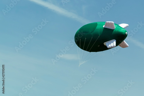 Green inflatable airship with a place for the logo on the background of blue sky with clouds. Mockup