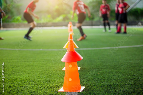 orange marker cones on green artificial turf for soccer training. Soccer equipment with blurry soccer team training