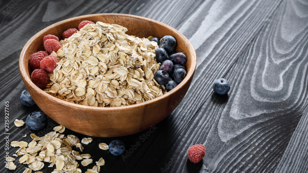 oatmeal with blueberries and raspberries in a wooden bowl on a black wooden table oatmeal with blueberries and raspberries in a wooden bowl on a black wooden table