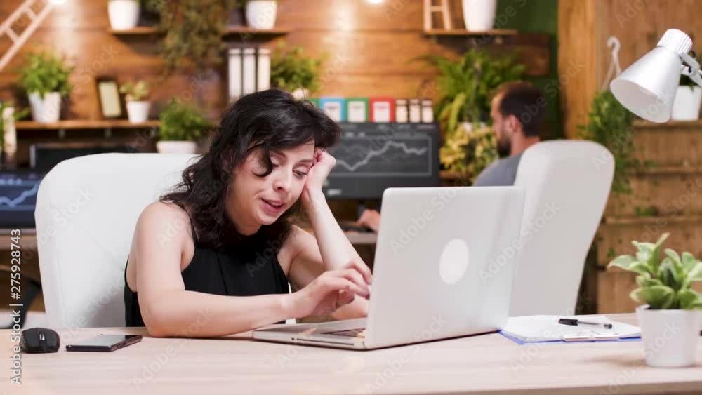 Tired and excited businesswoman works in cozy office. She yawns while working on the laptop