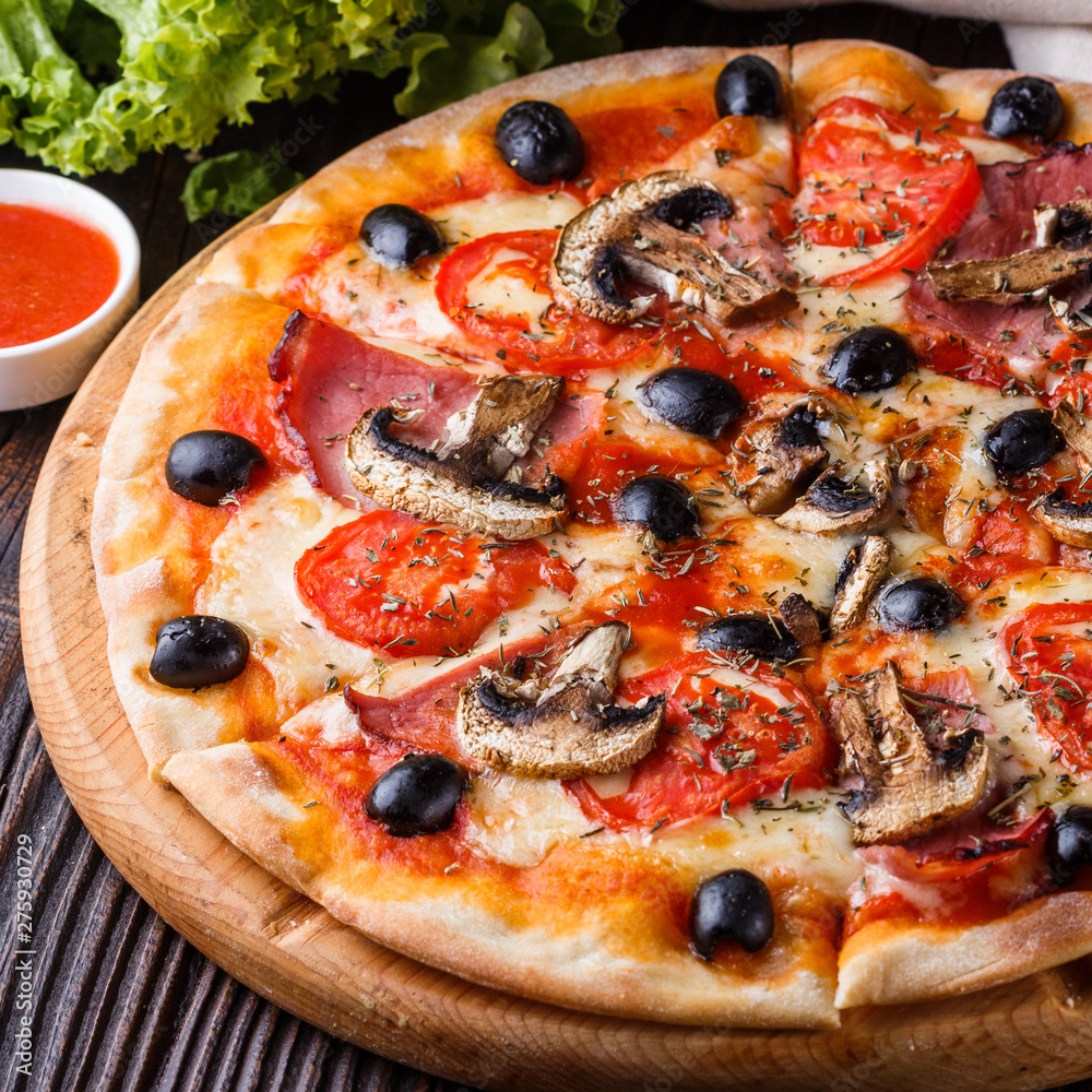 Pizza with tomato, olives, champignons, ham and cheese on round wooden plate Pizza with tomato, olives, champignons, ham and cheese on round wooden plate