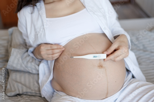Close-up of pregnant woman's abdomen with thermometer, temperature 36.6, health care in pregnancy