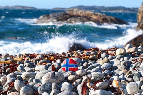 Image of the flag of Norway on a stone, between sea pebbles and seashells. Concept of Norwegian Constitution Day. Celebrated on May 17.