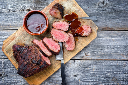 Barbecue dry aged wagyu tri tip steak with BBQ sauce as dip as top view on a wooden cutting board with copy space photo