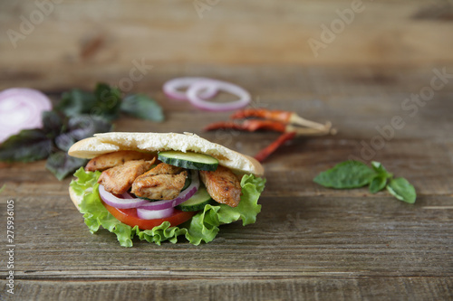 Closeup. Pita - sandwich, sabiche stuffed with chicken, tomatoes, cucumbers, salad on a wooden rustic background decorated with vegetables and pepper. Middle Eastern cuisine. With copy space for text. photo