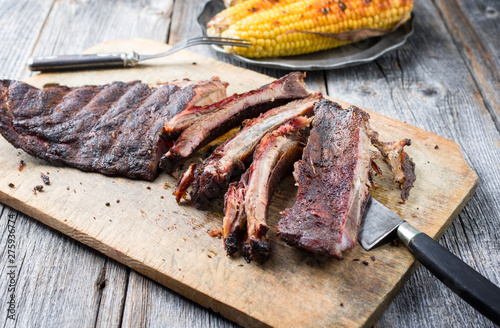 Barbecue spare ribs St Louis cut with hot rub and corn as closeup on a wooden cutting board