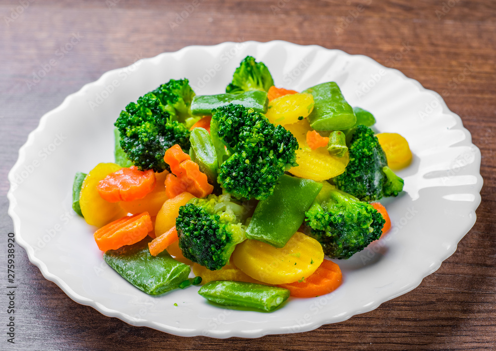 Mixed vegetables. green bean, broccoli and carrots in white plate on a wooden table background. 