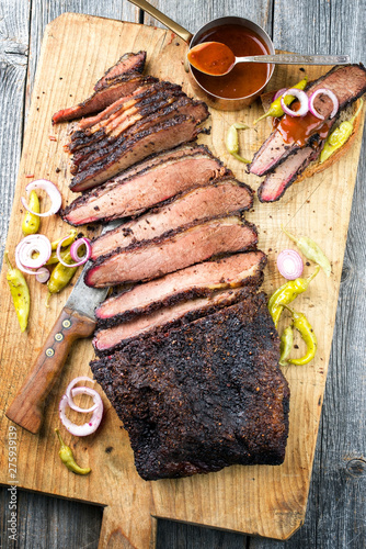 Traditional smoked barbecue wagyu beef brisket offered as top view on an old cutting board with Louisiana sauce onion rings and peperoni photo