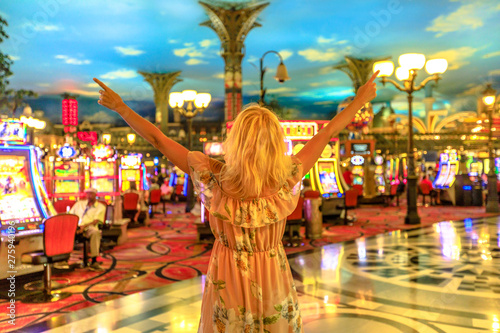 Happy winning caucasian woman at the casino of Las Vegas, Nevada, USA. Blonde lady enjoying spending money and being lucky enough to win. Architecture blur background. Gambling addict concept.