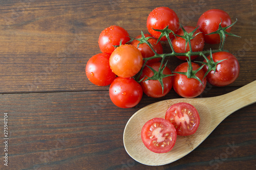 Fresh cherry tomatoes with branch and half cut tomatoes on wooden ladle on wooden background.