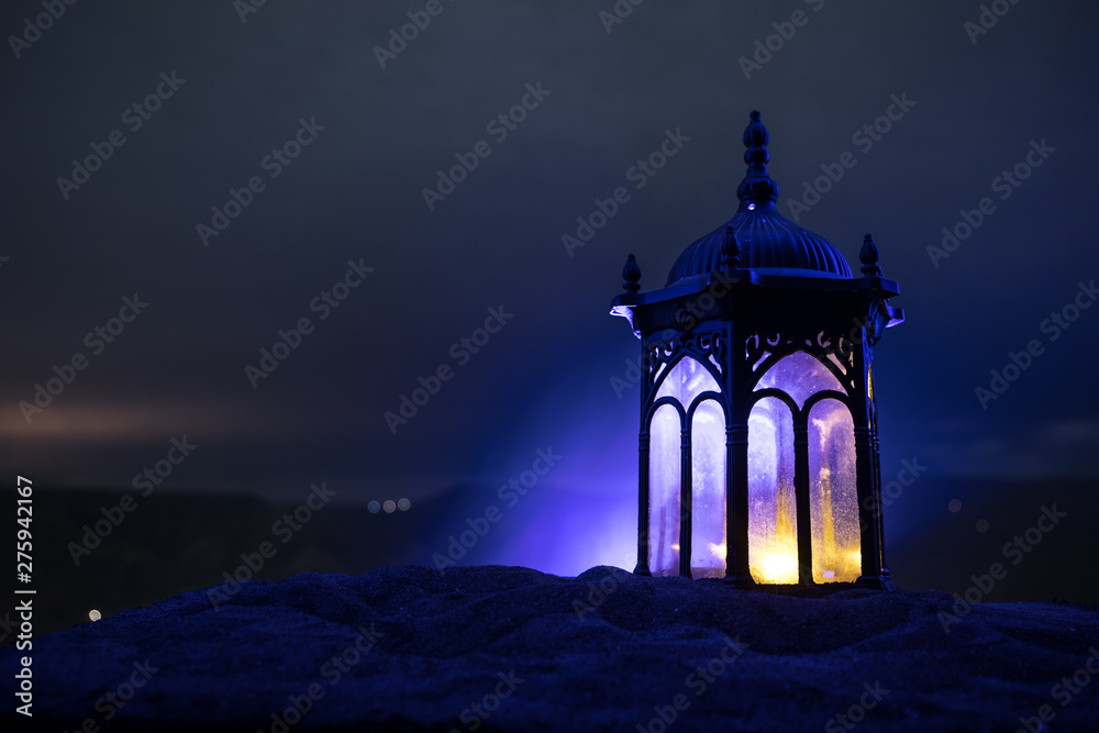 Fototapeta premium Ornamental Arabic lantern with burning candle glowing at night. Festive greeting card, invitation for Muslim holy month Ramadan Kareem.