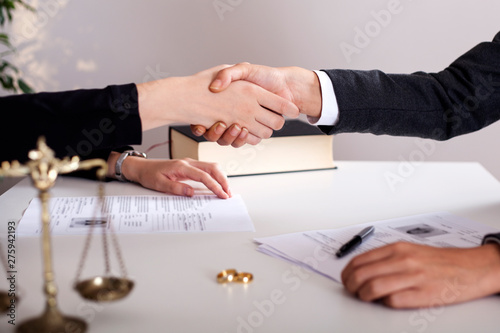partial view of lawyer and client sitting at table with divorce decree and wedding rings