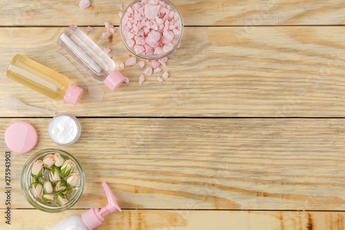 Face and body cosmetics in pink bottles with fresh roses on a natural wooden background. creams and lotion. spa. top view. space for your text