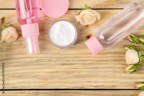 Fototapeta Naklejka Na Ścianę i Meble -  Face and body cosmetics in pink bottles with fresh roses on a natural wooden background. creams and lotion. spa. top view. space for your text
