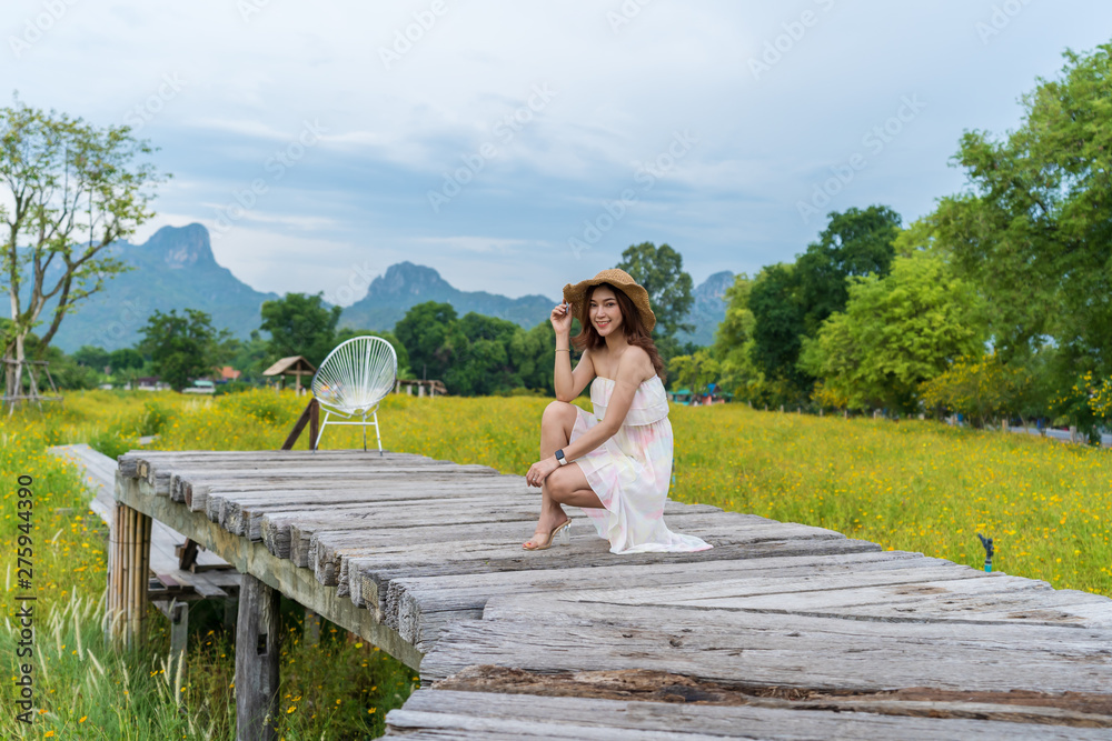 woman sitting on wooden bridge with yellow cosmos flower field