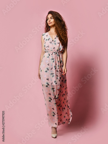 Slim curly female model in a silk pale pink dress looking at the camera in full growth. Cute girl in romantic clothes is going on a date