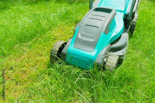  Lawn mower mowing green grass. Summer work in the garden.
