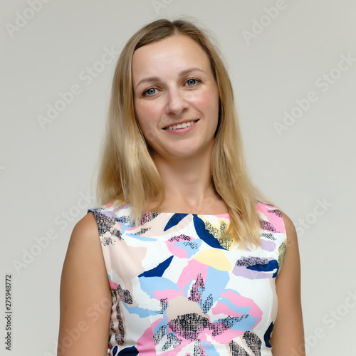 Portrait of a pretty beautiful adult female 35 years old blonde on a white background in a light dress with a pattern. Standing in front of the camera, smiling. photo