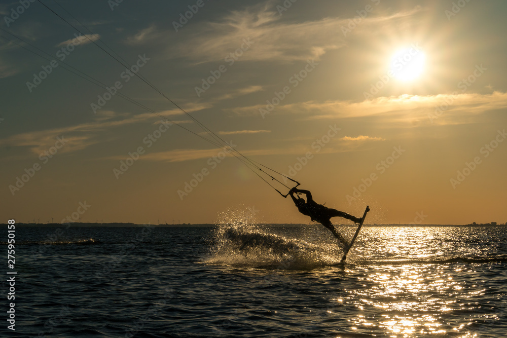 kitesurfer doing unhooked backroll in sunset with sunstar and beautiful silhouette