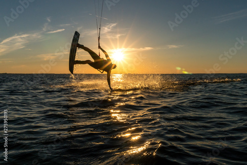 kitesurfer doing handslide in sunset with sunstar and beautiful silhouette
