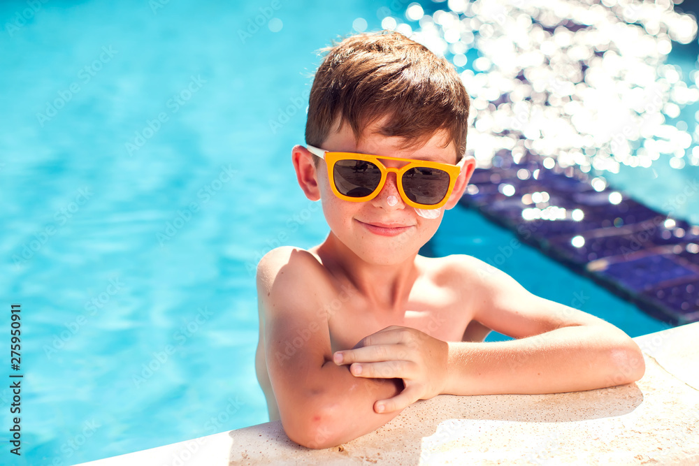 Kid boy with sun protection cream on his skin in the pool. Children, summer, holiday and healthcare concept
