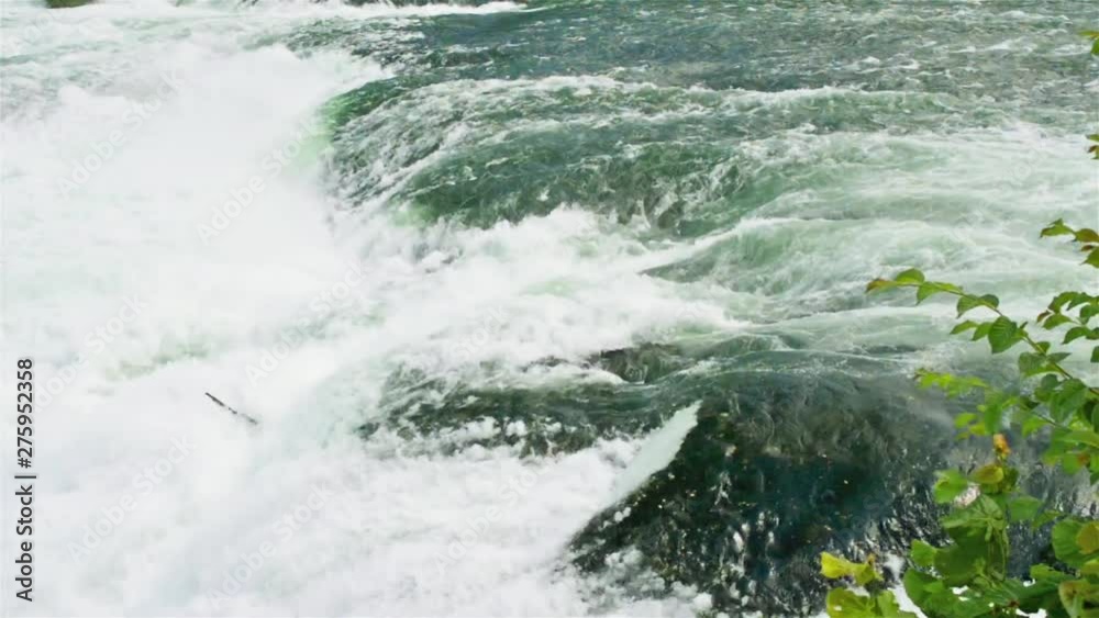 A beautiful view of a flowing, powerful waterfall, in the background fluttering the flag of Switzerland. Waterfall on the river Rhine in Neuhausen am Rheinfall in Switzerland. The largest waterfall in A beautiful view of a flowing, powerful waterfall, in the background fluttering the flag of Switzerland. Waterfall on the river Rhine in Neuhausen am Rheinfall in Switzerland. The largest waterfall in