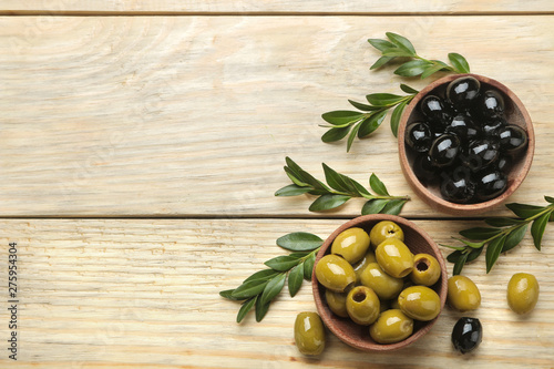 Green and black olives in a wooden bowl with leaves on a natural wooden table. top view. space for text