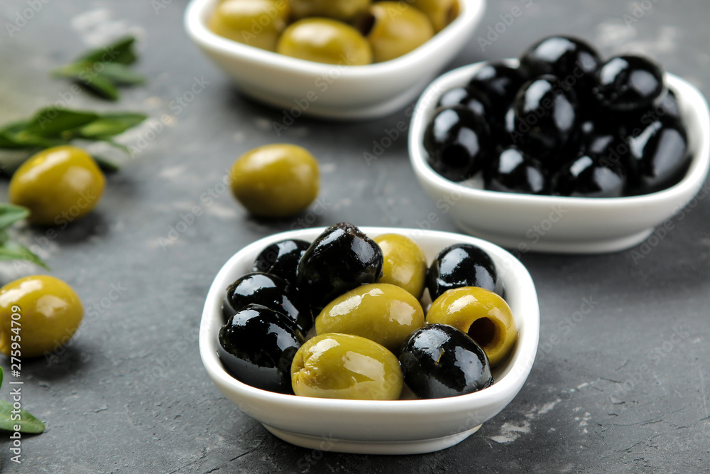 Green and black olives in a white ceramic bowl with leaves on a dark graphite background. close-up Green and black olives in a white ceramic bowl with leaves on a dark graphite background. close-up